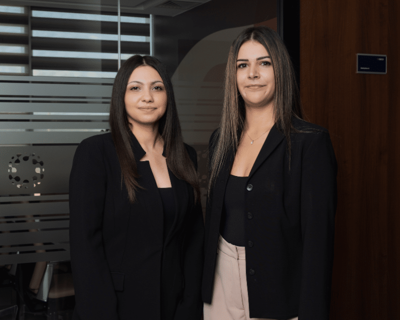 Cliona Testa Refalo and Chanel Borg looking at the camera in front of a glass wall.