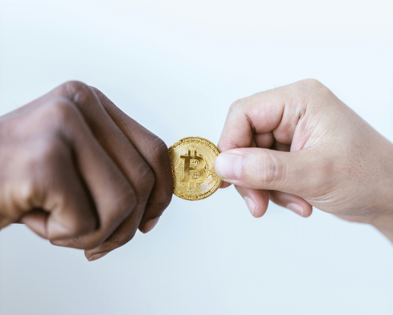 Two hands exchanging a physical Bitcoin coin, symbolising cryptocurrency transactions and digital asset exchange.