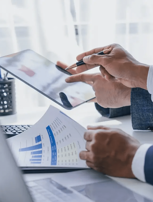 Close-up of business professionals reviewing financial charts and data on paper and a digital tablet.